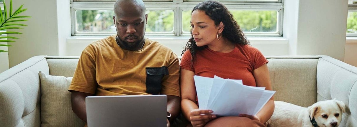 Man and woman sitting on the couch looking at a laptop with their dog.